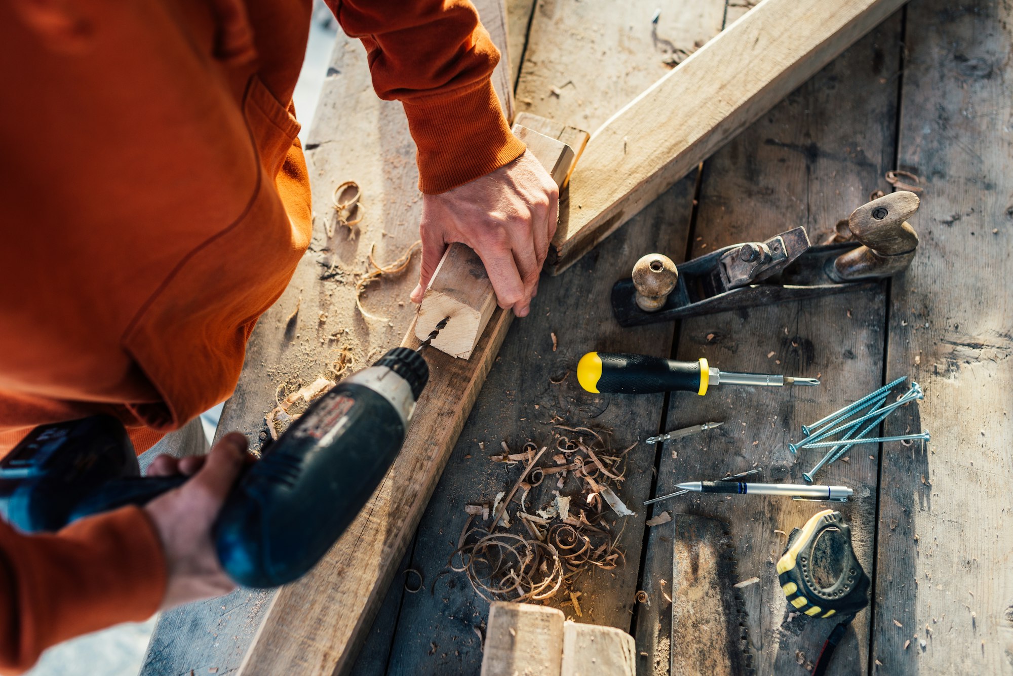 a worker drills a hole in wooden bar with drill