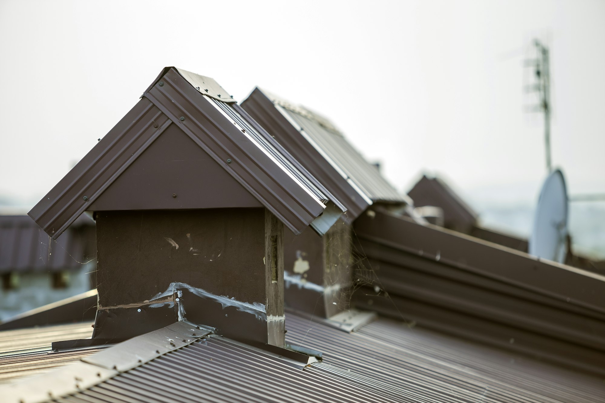 Close-up detail of new built brick plastered chimneys on house top with metal tile roof.